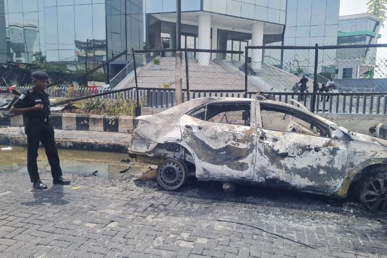 A Lagos policeman stands next to a burnt Rapid Response Squad car